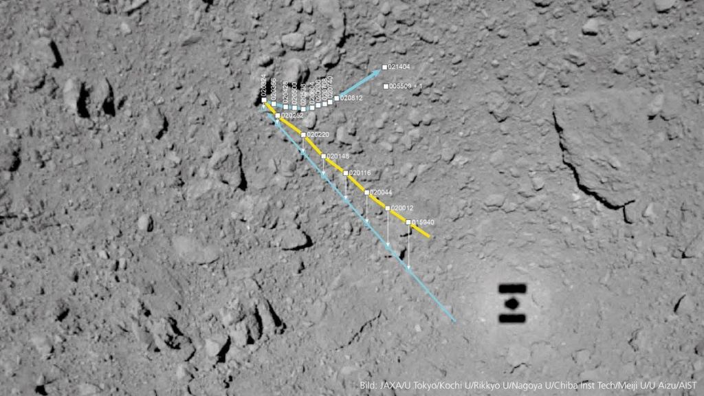 MASCOT's path across the surface of asteroid Ryugu. The path was recreated using data from the robot and from the mother probe Hayabusa2. Hayabusa2's shadow is visible at the bottim right. The yellow line is the robot's flight path down to the asteroid, and the blue line is the projection of these points onto Ryugu's surface. The blue line heading towards the right of the image is MASCOT's path along Ryugu's surface. Image Credit: DLR/JAXA