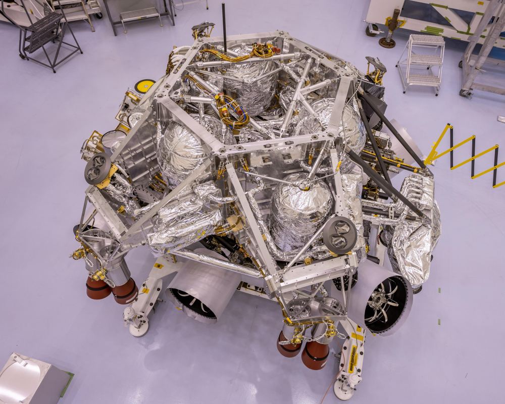NASA's Perseverance Rover in a clean room at Kennedy Space Center. The rocket-powered descent stage is sitting atop the rover, in this image from April 29th, 2020. This is the first step in the vehicle stacking process. Image Credit: NASA/JPL-Caltech