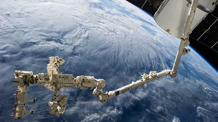 The International Space Station's Canadarm2 and Dextre carry the RapidScat instrument after removing it from the trunk of the SpaceX Dragon cargo ship (upper right). (Credit: NASA)