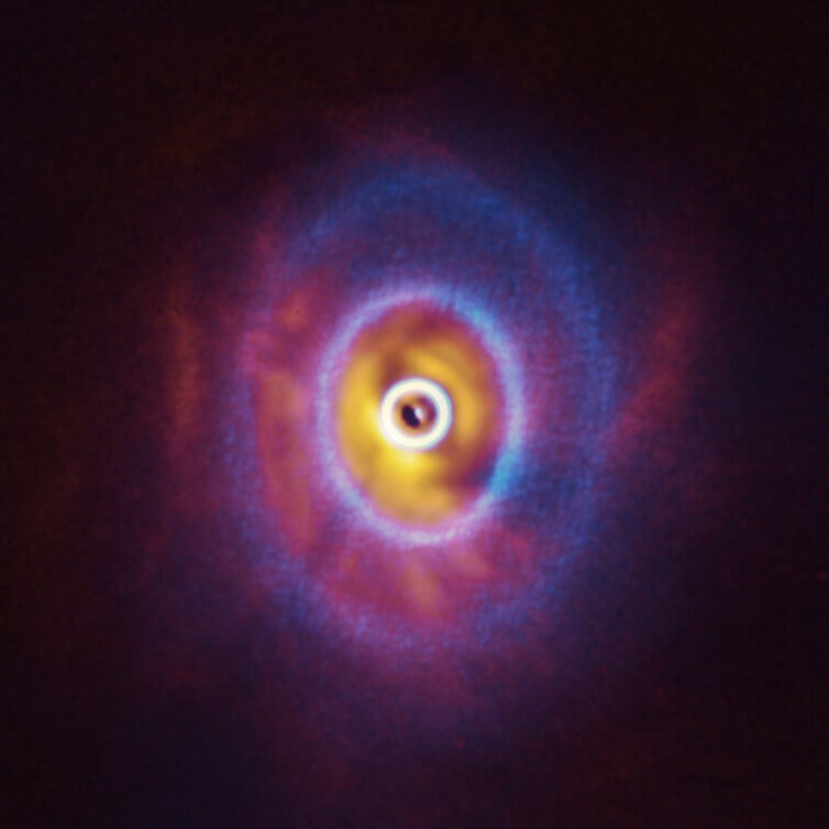 ALMA, in which ESO is a partner, and the SPHERE instrument on ESO’s Very Large Telescope have imaged GW Orionis, a triple star system with a peculiar inner region. Unlike the flat planet-forming discs we see around many stars, GW Orionis features a warped disc, deformed by the movements of the three stars at its centre. This composite image shows both the ALMA and SPHERE observations of the disc. The ALMA image shows the disc’s ringed structure, with the innermost ring (part of which is visible as an oblong dot at the very centre of the image) separated from the rest of the disc. The SPHERE observations allowed astronomers to see for the first time the shadow of this innermost ring on the rest of the disc, which made it possible for them to reconstruct its warped shape. Image Credit: ALMA (ESO/NAOJ/NRAO), ESO/Exeter/Kraus et al.