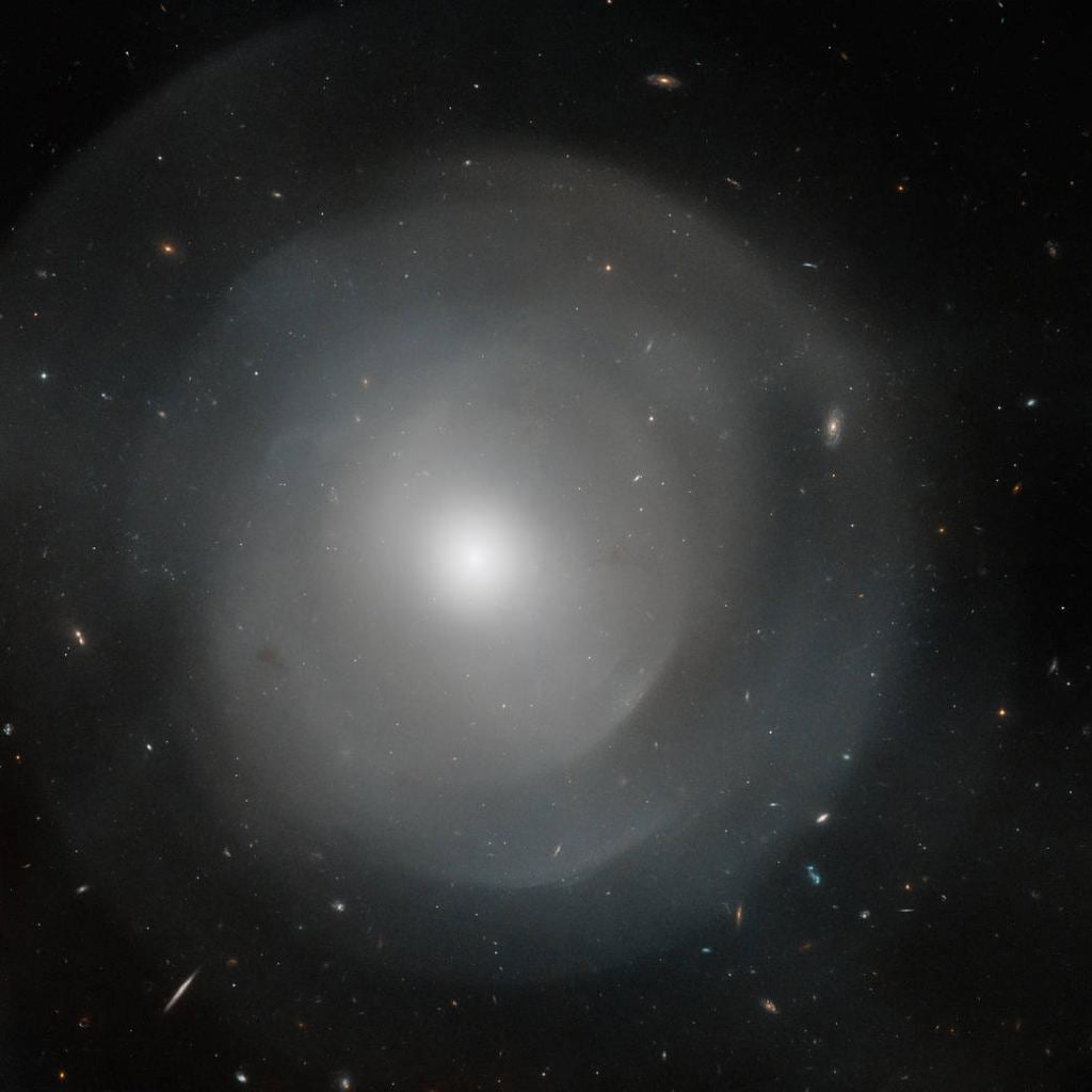 The central region of the giant elliptical galaxy NGC 474. It's set against a backdrop of more distant galaxies. Will the Milky Way resemble this galaxy in the distant future? This image was taken using the Hubble Advanced Camera for Surveys, and includes data from the Wide Field and Planetary Camera 3. (Courtesy NASA/STScI.)