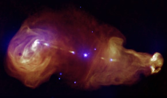 3C353 looks a bit like a tadpole. In the center of this image is a galaxy powered by a supermassive black hole, which is transmitting energy across the expanse. Radiation is visible in X-rays from Chandra (purple) and radio from the Very Large Array (orange.) Credit: X-ray: NASA/CXC/Tokyo Institute of Technology/J.Kataoka et al, Radio: NRAO/VLA