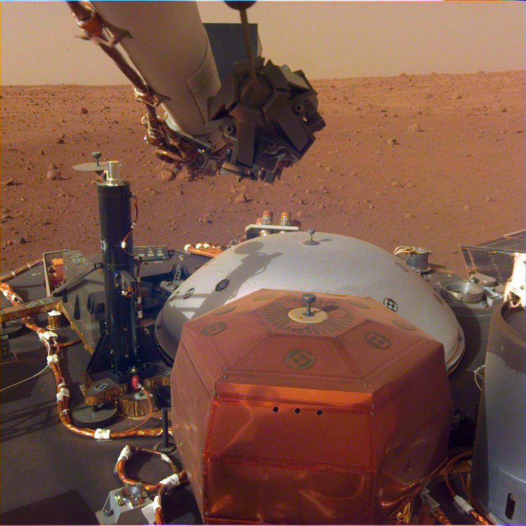 This image was taken by the InSight Lander's Instrument Deployment Camera mounted on the lander's robotic arm. The stowed grapple on the end of the arm is folded in, but it will unfold and be used to deploy the lander's science instrument. The copper-colored hexagonal object is the protective cover for the seismometer, and the grey dome behind it is a wind and thermal shield, which will be placed over the seismometer after its deployed. The black cyliner on the left is the heat probe, which will drill up to 5 meters into the Martian surface. Image: NASA/JPL-Caltech