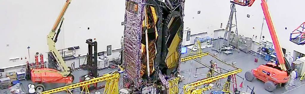 A webcam image of the JWST fully stowed into the same configuration it will have when loaded into an Ariane V rocket for launch. It's in a clean room at Northrop Grumman, in Redondo Beach, California. Image Credit: Northrop Grumman.