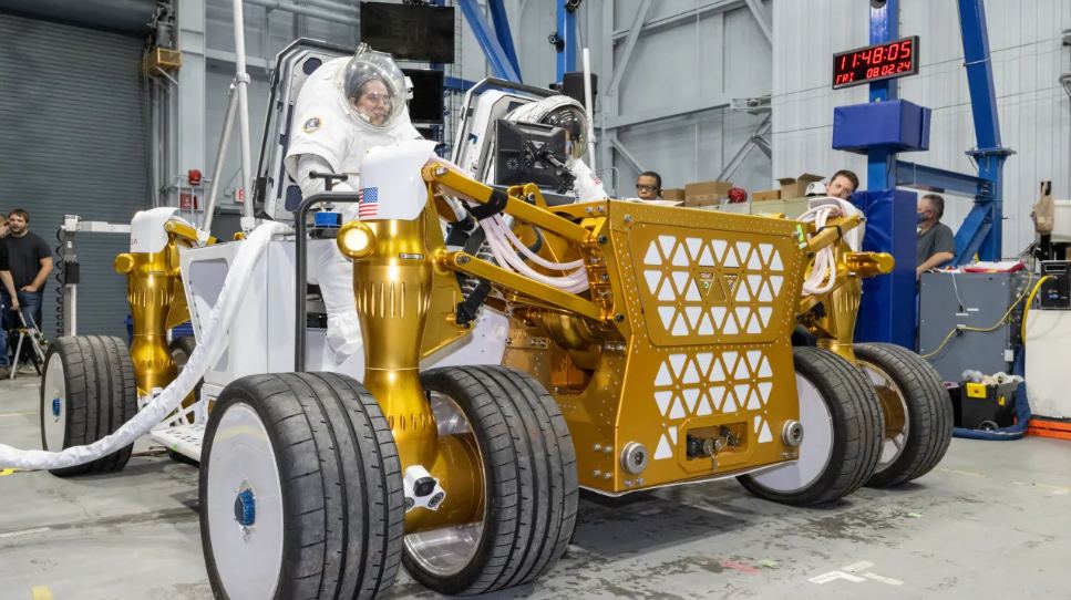 Two engineers in suits sit on the prototype during testing at the Johnson Space Center. Image Credit: NASA/Bill Stafford