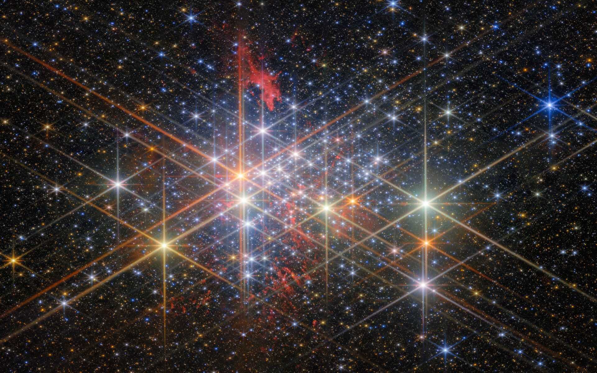 Here's Westerlund 1 in all its glory. This dense cluster of bright stars (with diffraction spikes from JWST's optics). They have a variety of sizes depending on their brightness and distance from us in the cluster, and different colors reflecting different types of star. Patches of billowing red gas can be seen in and around the cluster, lit up by the stars. Small stars in the cluster blend into a background of distant stars and galaxies on black. Courtesy ESA/Webb NASA & CSA, M. Zamani (ESA/Webb), M. G. Guarcello (INAF-OAPA) and the EWOCS team.