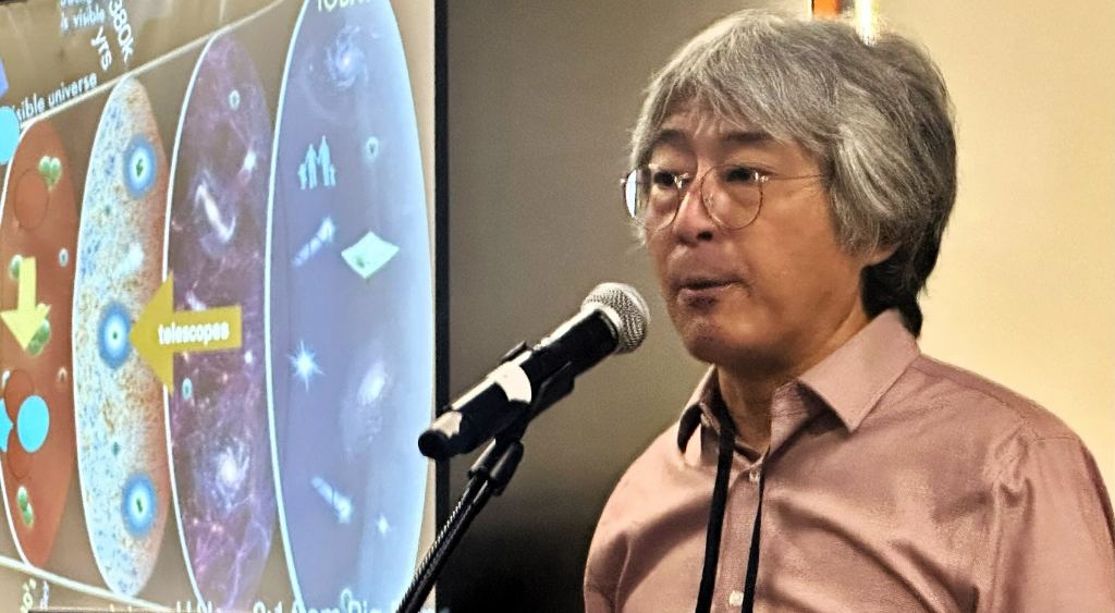 Hitoshi Murayama with slide charting the history of the universe in the background